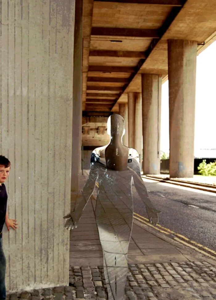 Transparent reflective sculpture under a bridge with a child nearby