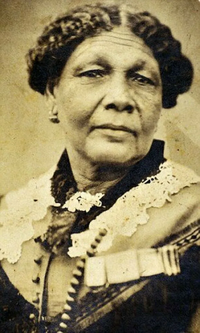 A sepia-toned oval portrait of a woman with dark curly hair and a lace collar, featuring a medal, celebrating women in history.