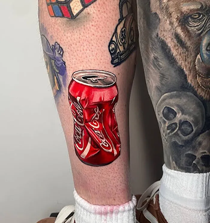 Crushed Coca-Cola can tattoo on calf surrounded by other tattoos