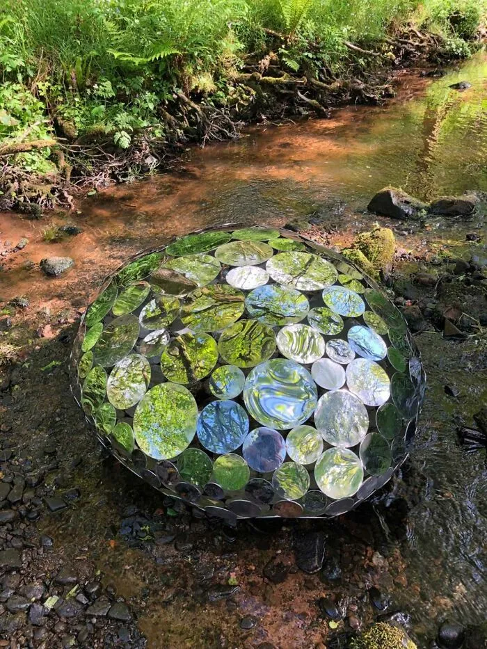 Reflective sculpture made of circular mirrors resting in a woodland stream