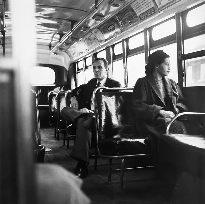 Rosa Parks sits on a bus with a man, a pivotal moment for Women In History.