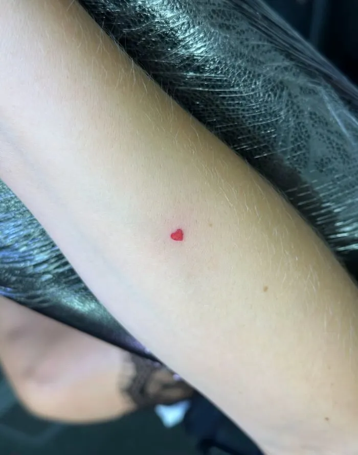 Tiny red heart tattoo on inner forearm with simple design