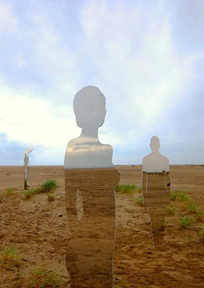 Group of reflective sculptures on a sandy beach blending with natural surroundings