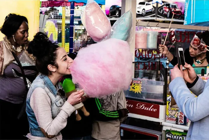 A street photographer captured an odd coincidence: a young woman laughing while eating cotton candy, with other people around.