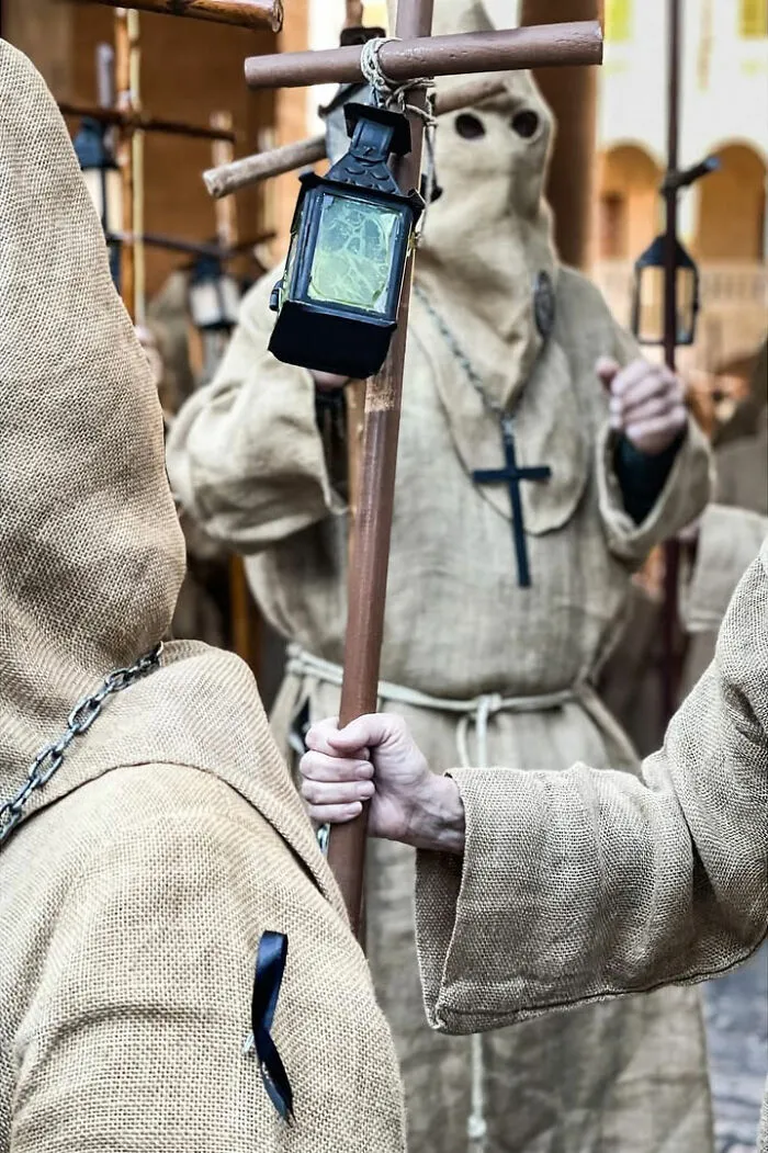 A street photographer captures hooded figures holding a cross and lanterns, an odd and intriguing street scene.