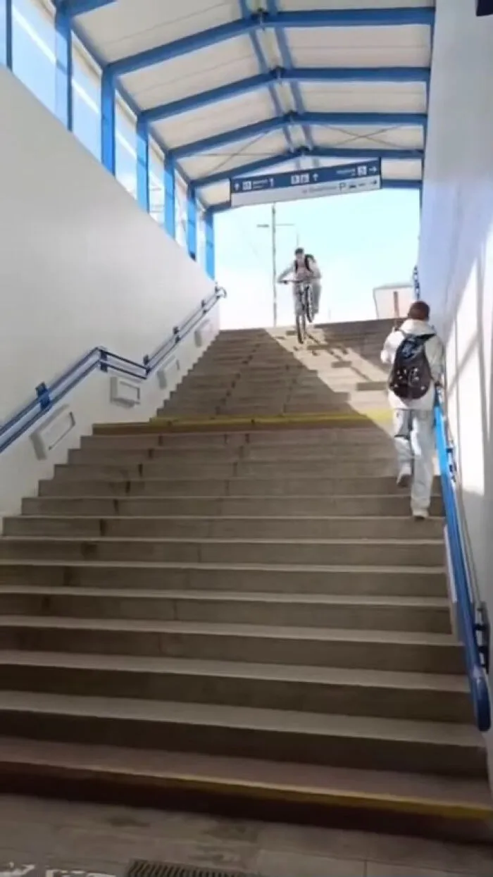 A man with a backpack walks up stairs while a main character cyclist rides down.