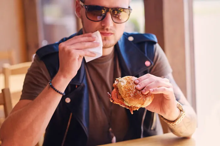 A man wiping his mouth while holding a burger, showing cheap meal choices