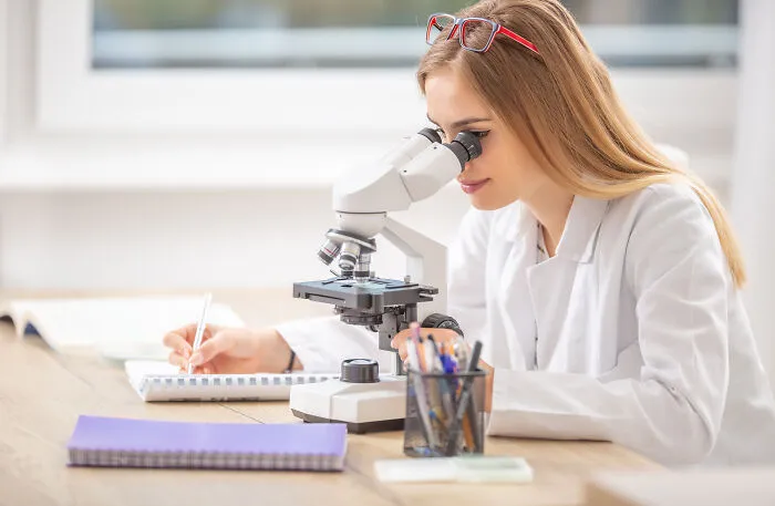 Young woman looking through a microscope, reflecting life paths of smart kids.