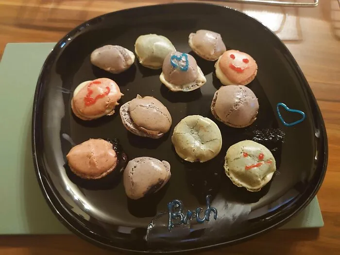 Unsuccessful macaron baking with cracked shells on black plate