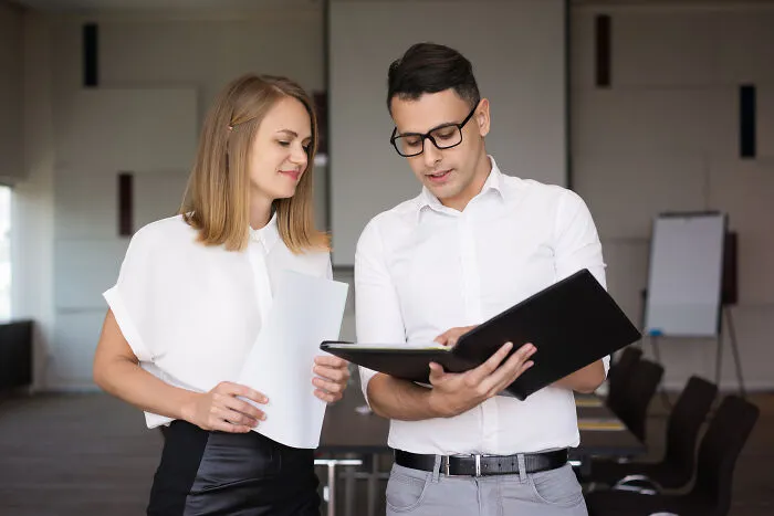 A female office worker holds documents while a male colleague looks on, representing subtle sexism.