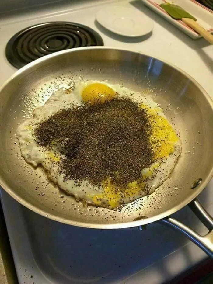 Fried eggs covered with excessive black pepper in pan
