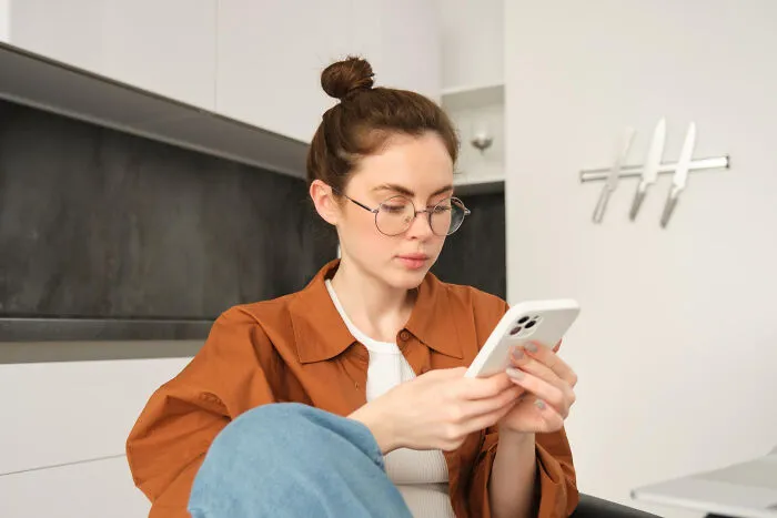 A woman in glasses looks at her smartphone, illustrating unsettling and creepy things confessed online.