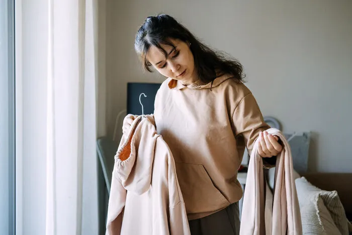A woman holding up similar-looking hoodies, symbolizing creepy habits with a partner.