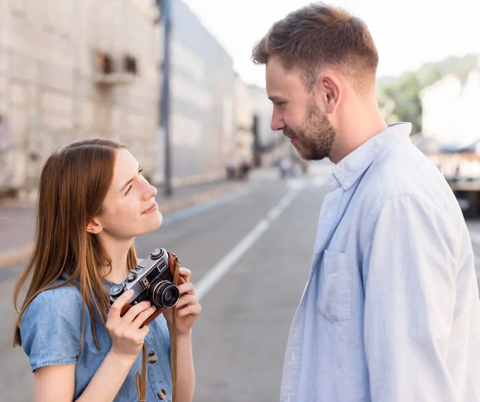 A young woman with a camera looking up at her partner on a street.
