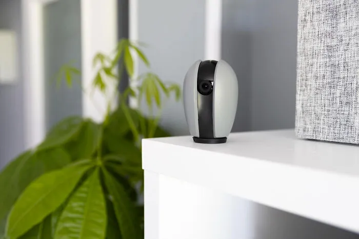 A small gray and black indoor security camera sits on a white shelf, hinting at unsettling and creepy things.