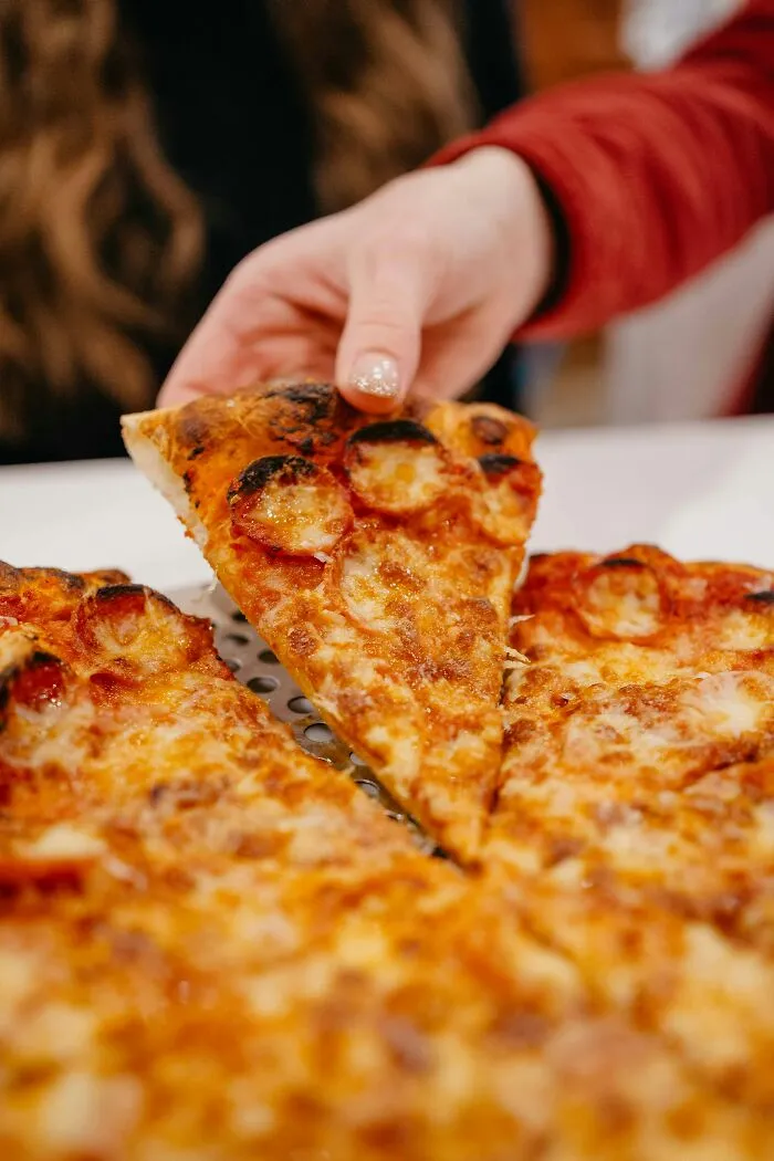 A hand picking up a single slice of pepperoni pizza from a whole pie, illustrating cheap food choices.