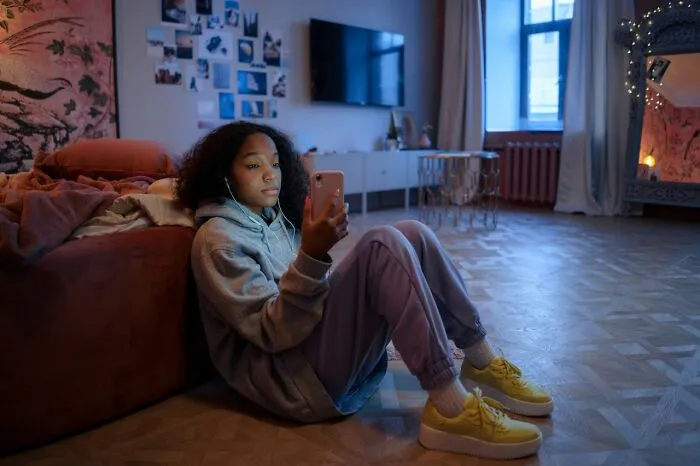 Young woman in hoodie looking at phone feeling isolated from family