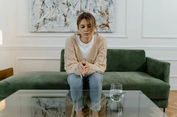 Sad woman sitting alone on couch reflecting on family cut off reasons