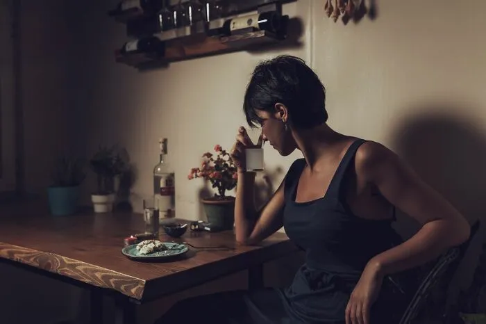 Woman drinking alone at table, symbolizing family cut off pain