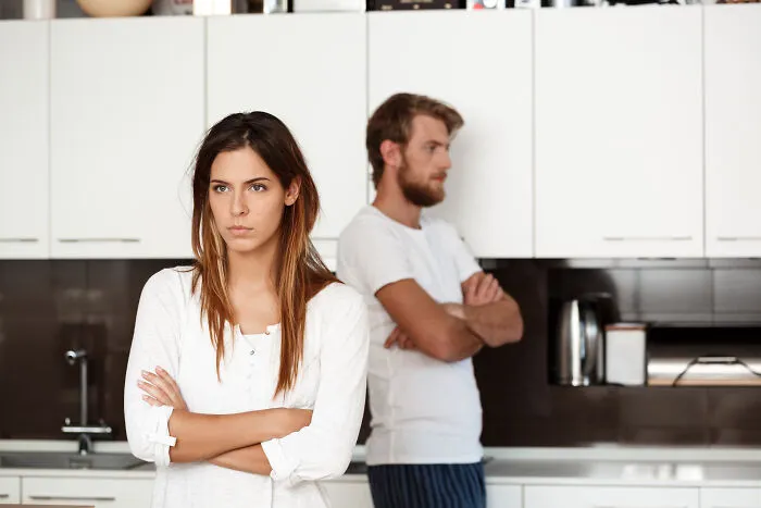 An unhappy couple standing in a kitchen with arms crossed, showing signs of marriage regrets