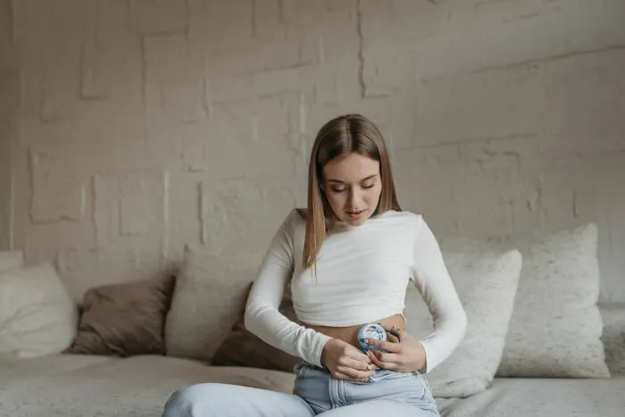 A woman uses a medical device on her abdomen, showing a patient with medical education needs.