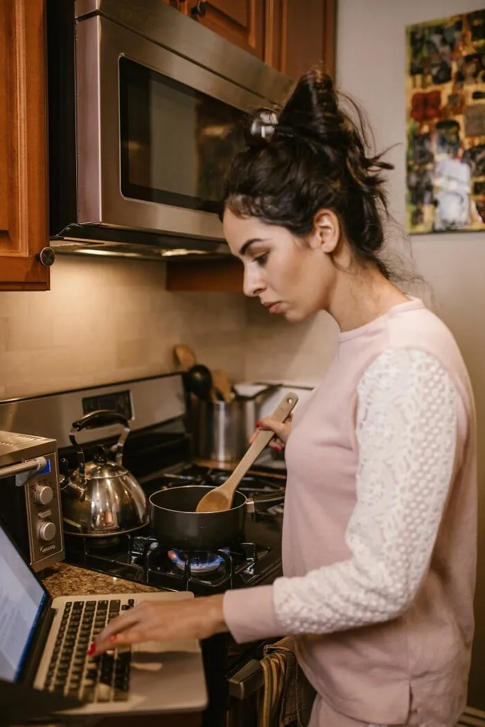 A woman cooking while using her laptop, showing habits that make men lose interest in a woman