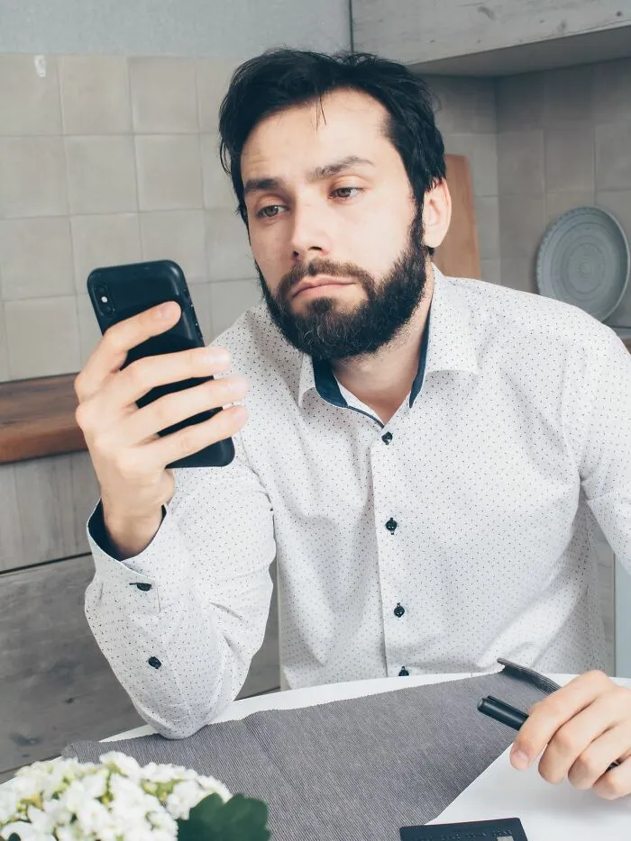 A bored man stares at his phone, realizing why men lose interest in a woman instantly over minor details