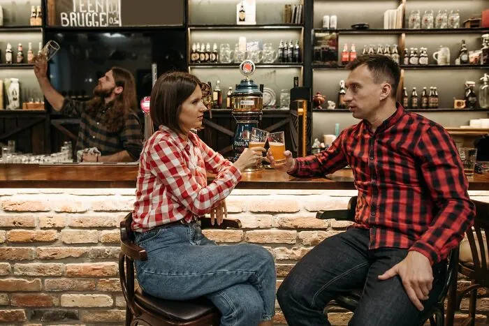 A couple toasts drinks at a bar, highlighting how men lose interest in a woman instantly over simple habits