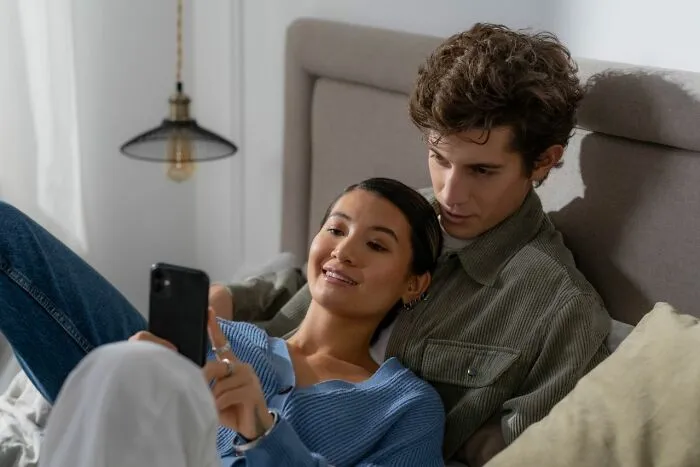 A couple looking at a smartphone in bed, showing modern habits that make men lose interest.