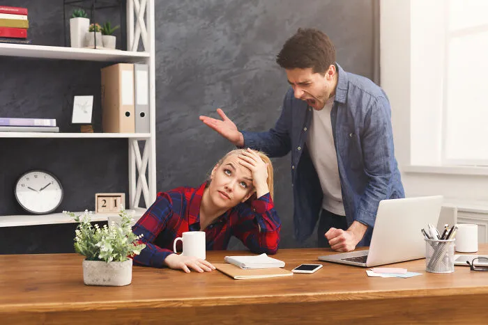 A frustrated woman at her desk, showcasing subtle sexism from a male colleague who is shouting