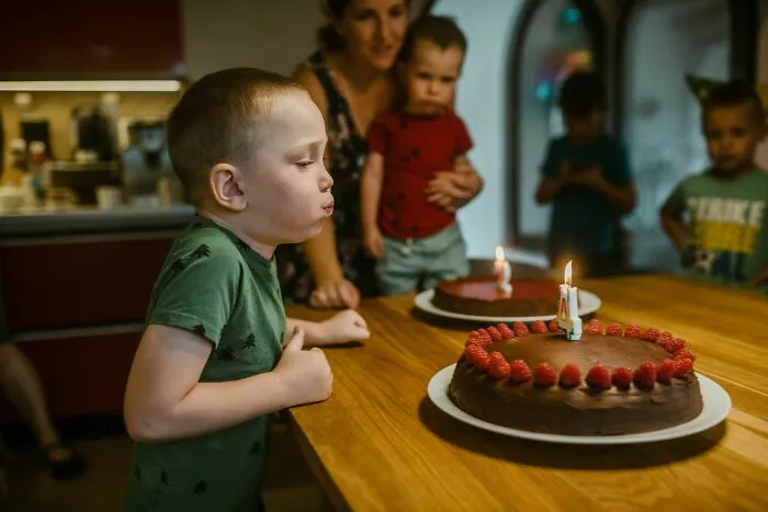 A young boy blowing out a candle on a chocolate birthday cake, illustrating stories of entitled parents.