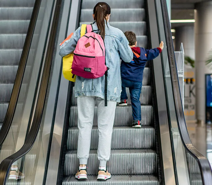 A woman with a pink backpack on an escalator with a child, showing a scene relevant to entitled parents.