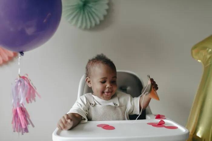 A happy toddler sitting in a high chair with balloons, a common focus of entitled parents stories.