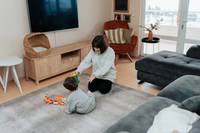 A mother playing with her young child on a living room rug, highlighting the challenges faced by parents