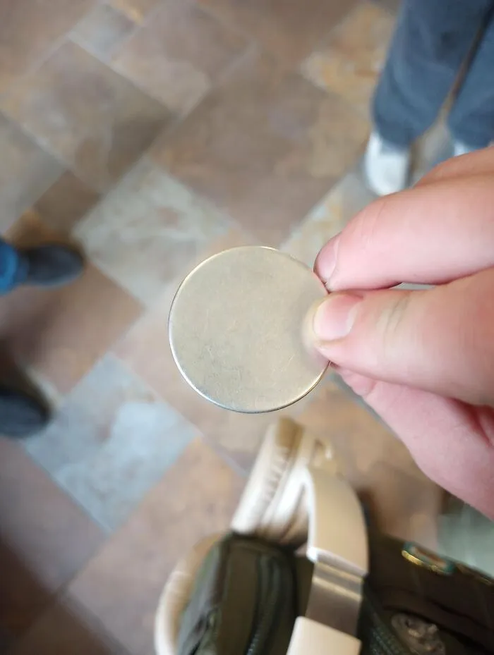 A hand holding a completely smooth and blank silver coin, showing how time slowly reshapes metals.