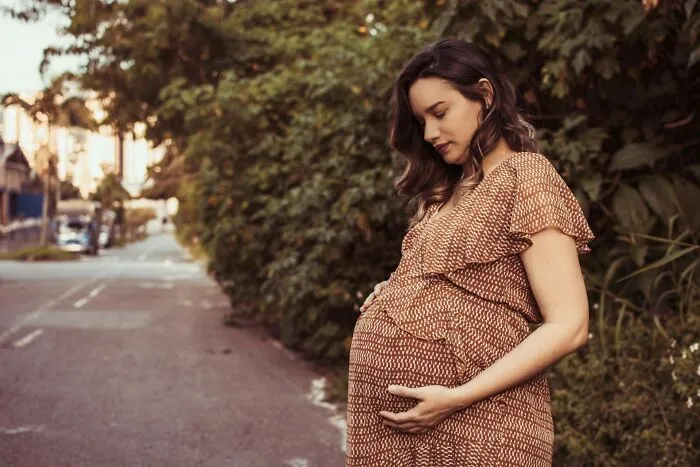 A pregnant woman in a patterned dress holding her belly outdoors, reflecting maternal health medical practices
