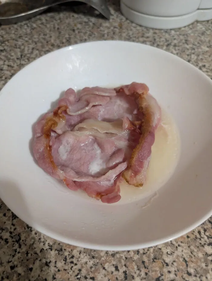 A piece of cooked bacon served in a bowl of milk, showing a bizarre food combination