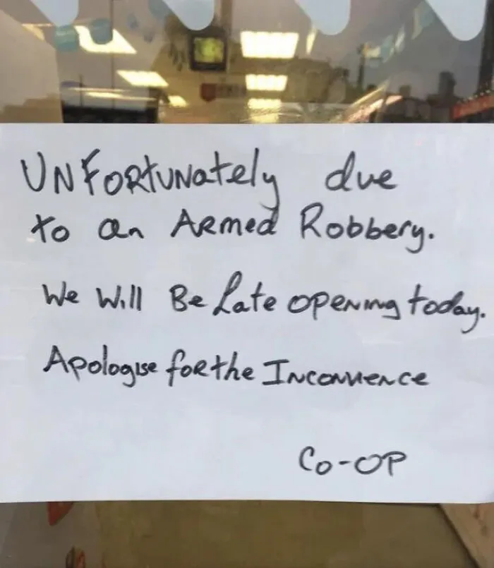 Handwritten sign on a door apologizing for late opening due to an armed robbery, showing signs from around the world.