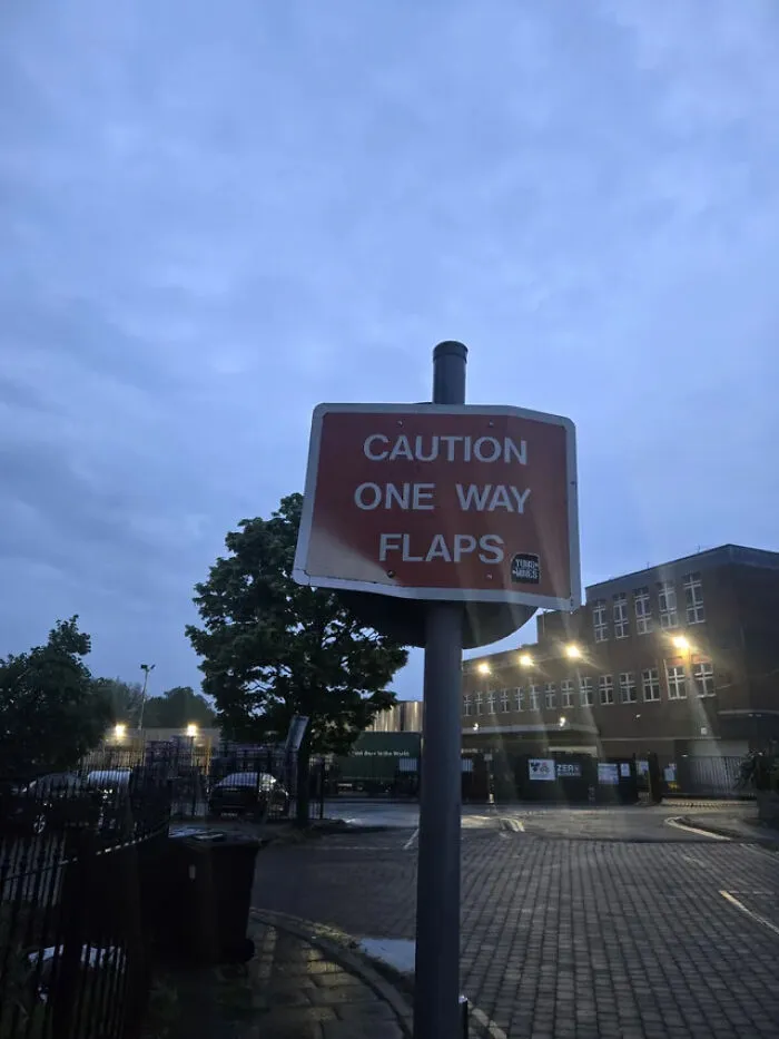 An street sign reading Caution One Way Flaps in an industrial area, highlighting funny signs from around the world.