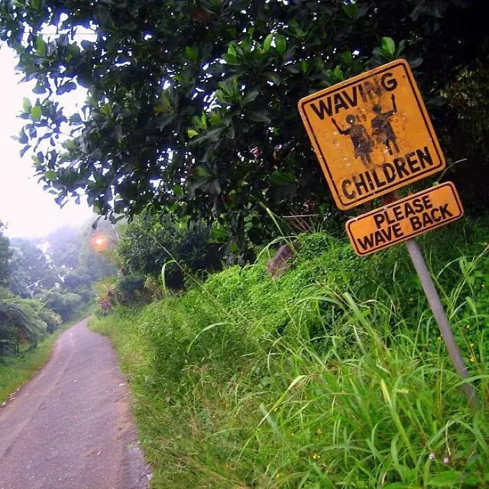 A yellow roadside sign saying Waving Children Please Wave Back, showing funny mistakes on signs