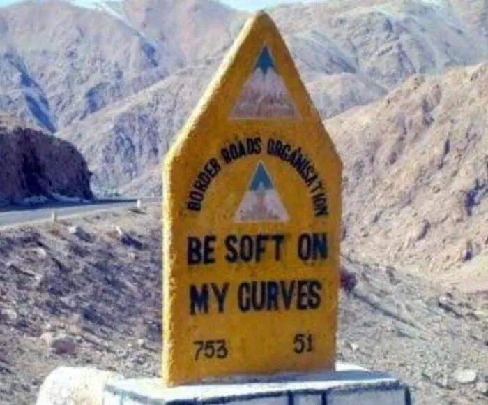 A yellow concrete road milestone with a humorous message, displaying unique signs from around the world.