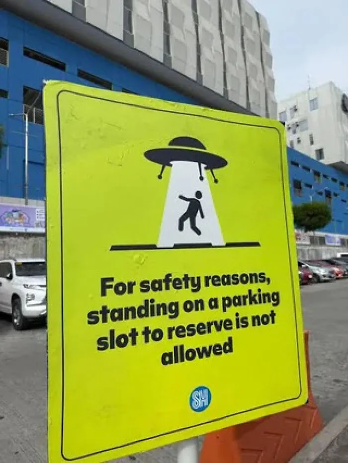 A bright yellow sign with an illustration of a UFO abducting a person, warning about parking rules.