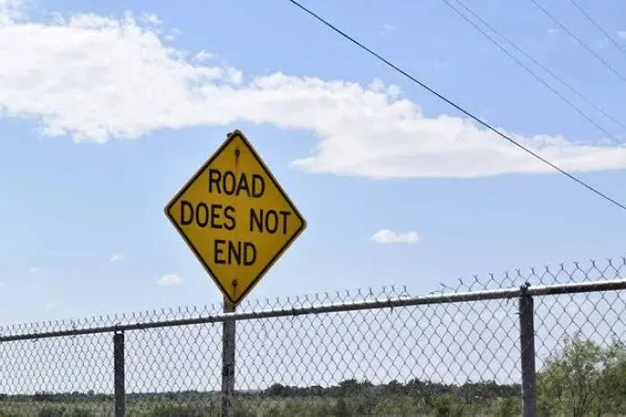 A yellow diamond road sign stating Road Does Not End, showing a funny design mistake.