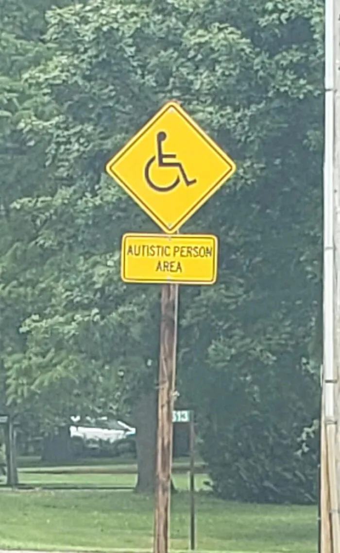 An unusual street sign reading Autistic Person Area with a wheelchair symbol, showing a sign mistake.