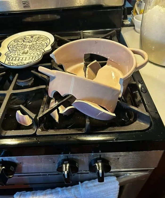 Shattered pink ceramic pot on a black gas stovetop next to a decorative skull plate, a dramatic kitchen fail.