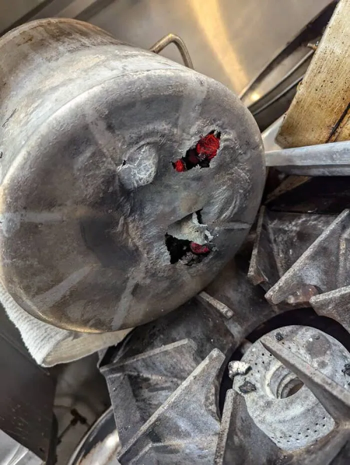 Close-up of a melted aluminum pot with holes, a kitchen fail showing fire damage on a stovetop.