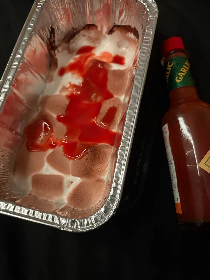 Toasted marshmallows in a foil container topped with hot sauce, demonstrating odd food combinations