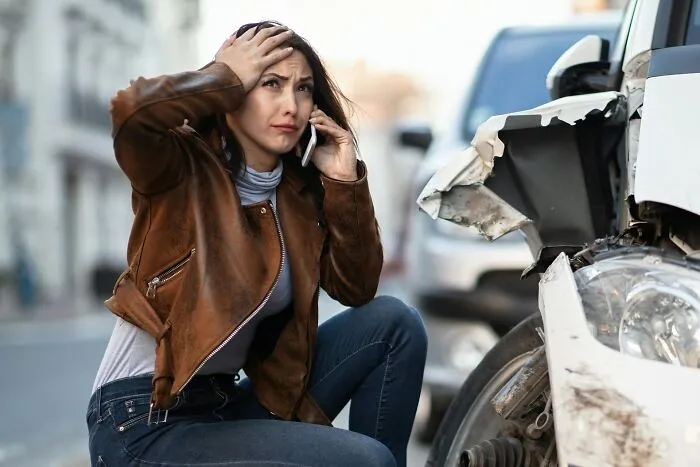 A worried woman on the phone next to a crashed car, demonstrating tips for an emergency