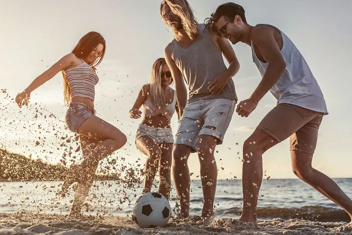 Group of friends playing soccer on beach during vacation