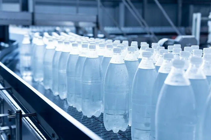 Rows of bottled water on a factory conveyor belt, referencing corporate scandals